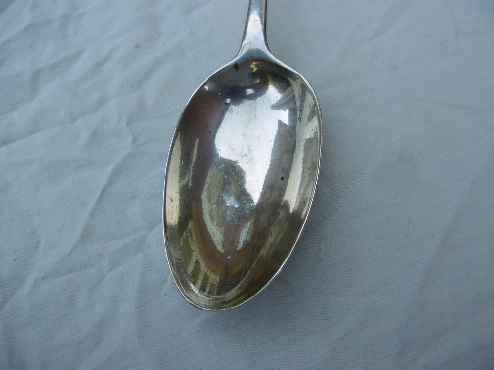 An 18th-century Irish Georgian sterling silver basting spoon featuring a tapered stem with an engraved family crest and a distinctive hooked handle terminal. View VI