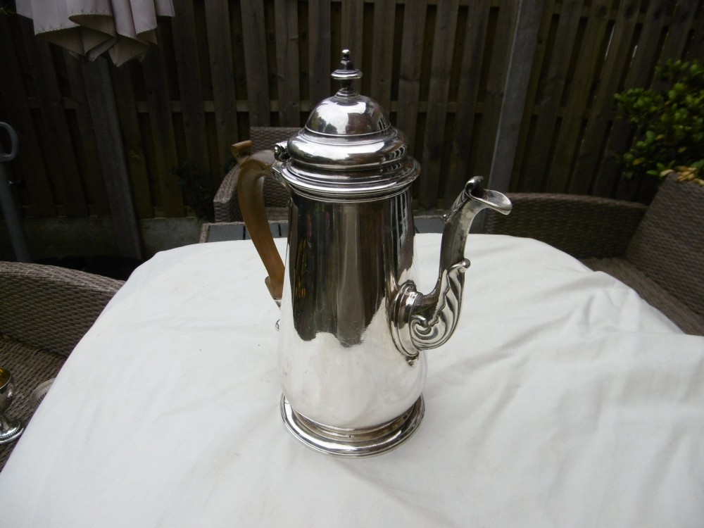 A George II sterling silver coffee pot with a tapered body, domed lid, decorative cast spout, and a curved wooden handle.
