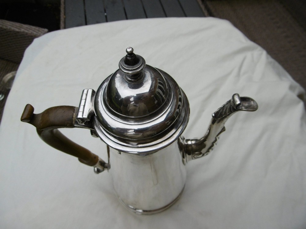 A George II sterling silver coffee pot with a tapered body, domed lid, decorative cast spout, and a curved wooden handle. View V