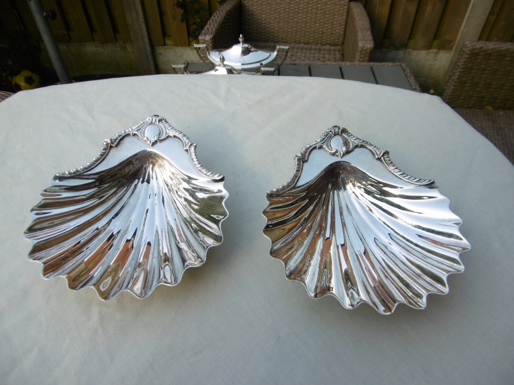 A pair of 18th-century sterling silver butter dishes shaped like scallop shells with fluted interiors and engraved handles.