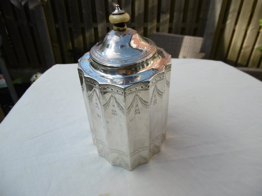 A George III fluted sterling silver tea caddy featuring bright-cut engraved drapery swags, a central keyhole, and a hinged lid topped with a turned finial. View II