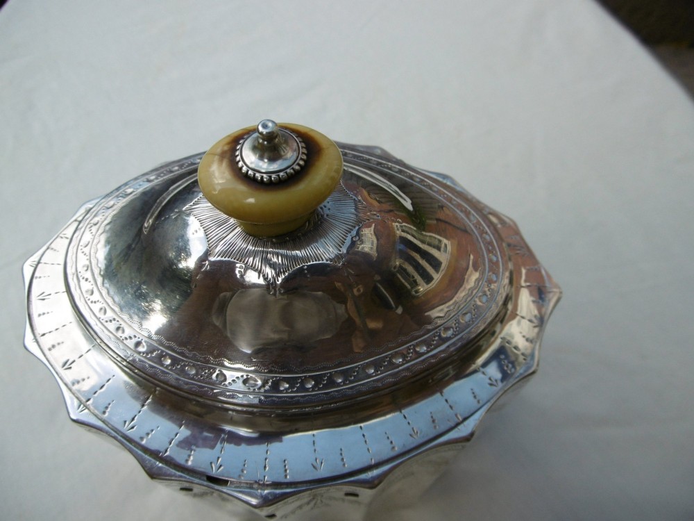 A George III fluted sterling silver tea caddy featuring bright-cut engraved drapery swags, a central keyhole, and a hinged lid topped with a turned finial. View VI