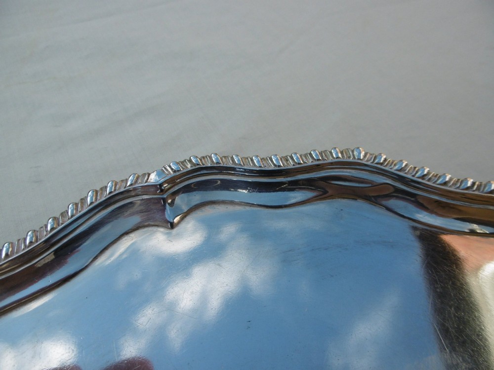 A circular Georgian sterling silver salver featuring a scalloped gadrooned rim and a central armorial crest engraving. View IV