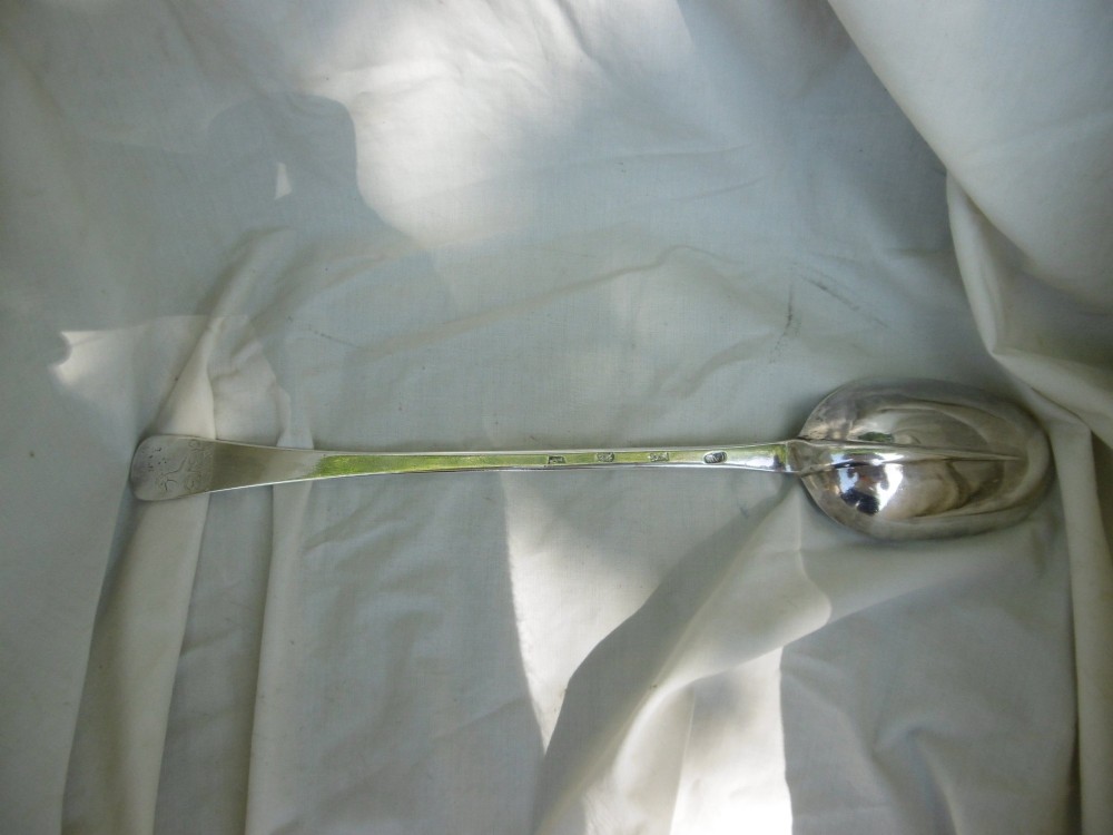 A long George I sterling silver hash spoon featuring an elongated oval bowl resting on white fabric. View II