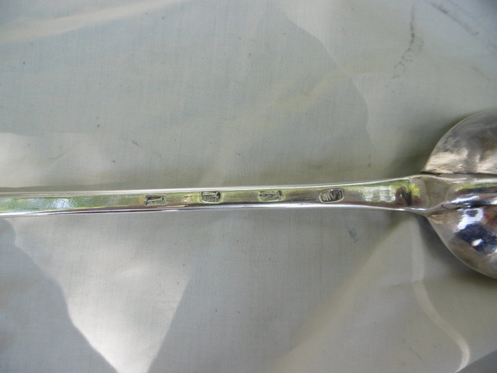 A long George I sterling silver hash spoon featuring an elongated oval bowl resting on white fabric. View III