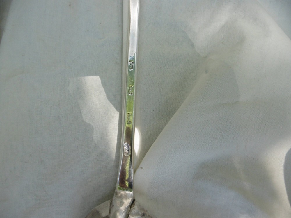 A long George I sterling silver hash spoon featuring an elongated oval bowl resting on white fabric. View IV