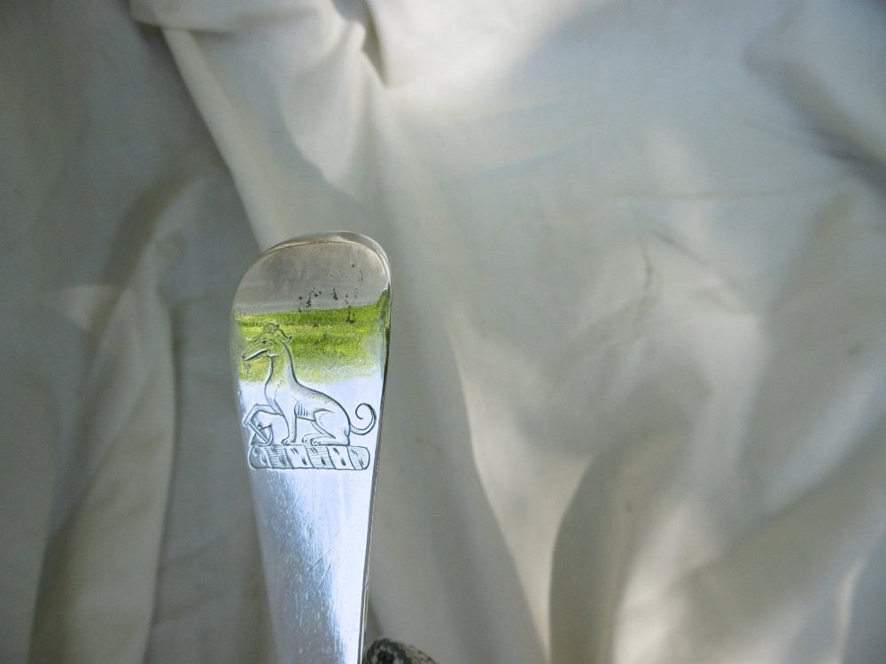 A long George I sterling silver hash spoon featuring an elongated oval bowl resting on white fabric. View V