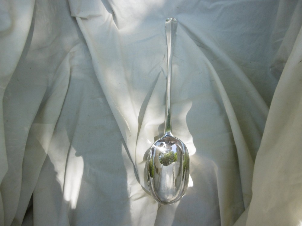 A long George I sterling silver hash spoon featuring an elongated oval bowl resting on white fabric. View VI