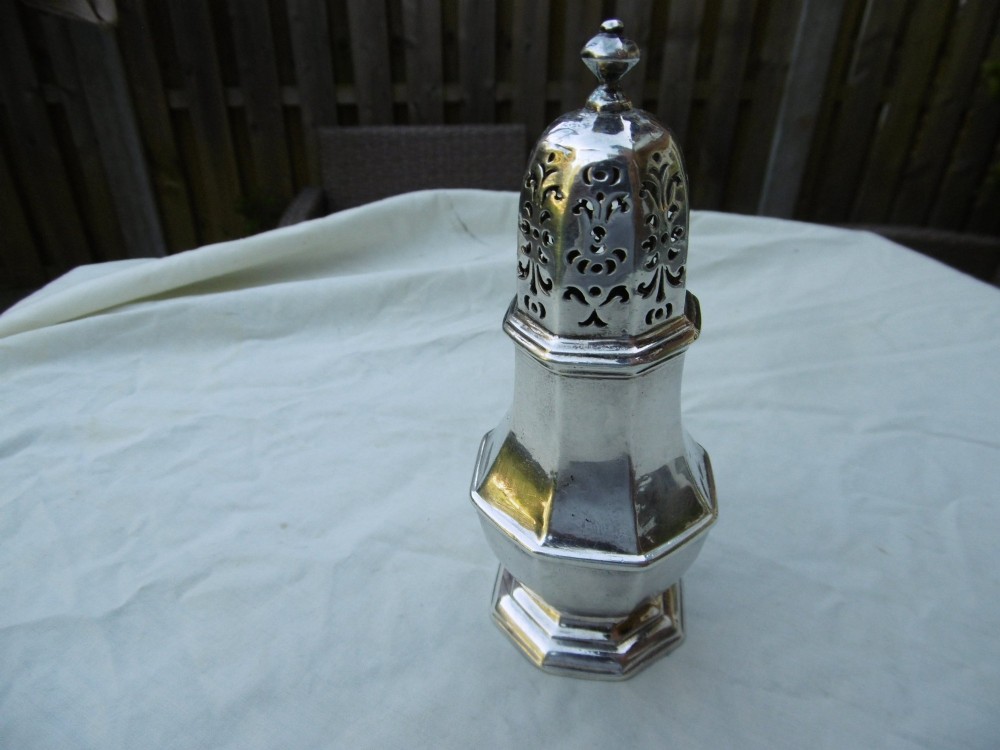 An 18th-century octagonal sterling silver sugar caster featuring a baluster-shaped body, moulded foot, and intricate pierced dome lid topped with a finial.