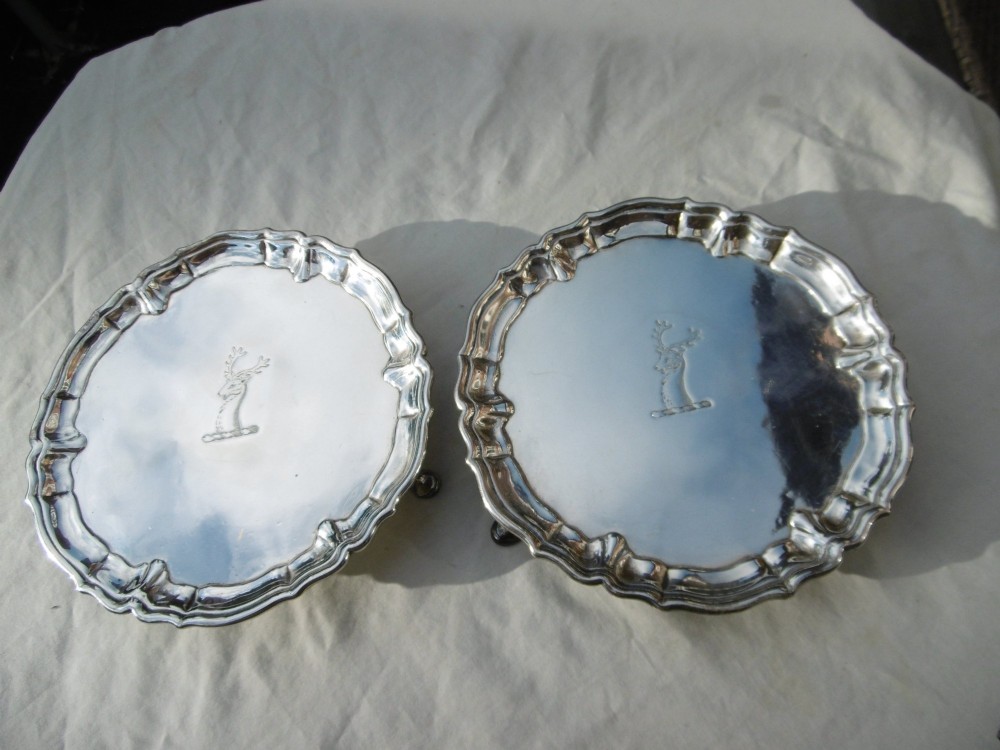 A pair of round George II sterling silver waiters with piecrust borders, resting on small feet, each central panel engraved with a stag crest.