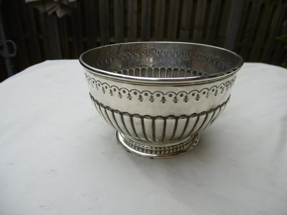 A George III sterling silver footed bowl featuring a fluted lower body, an engraved foliate upper border, and a stepped circular base.
