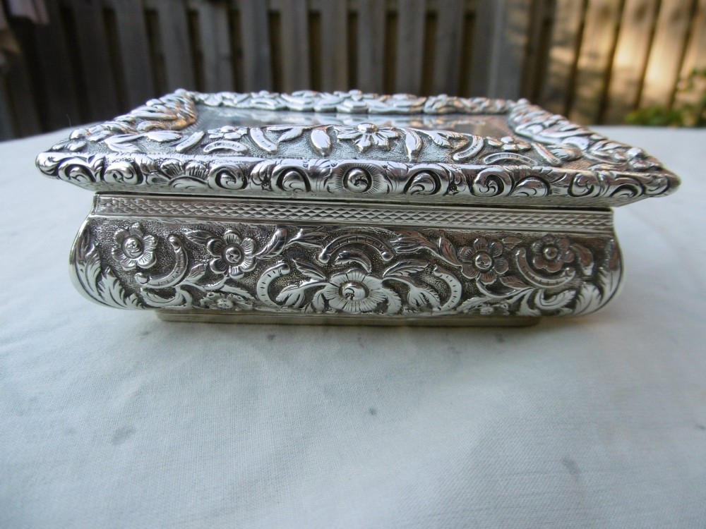 A rectangular William IV sterling silver table snuff box featuring heavily chased floral borders and an engine-turned lid with a plain central cartouche. View II