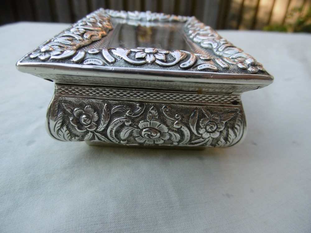 A rectangular William IV sterling silver table snuff box featuring heavily chased floral borders and an engine-turned lid with a plain central cartouche. View III