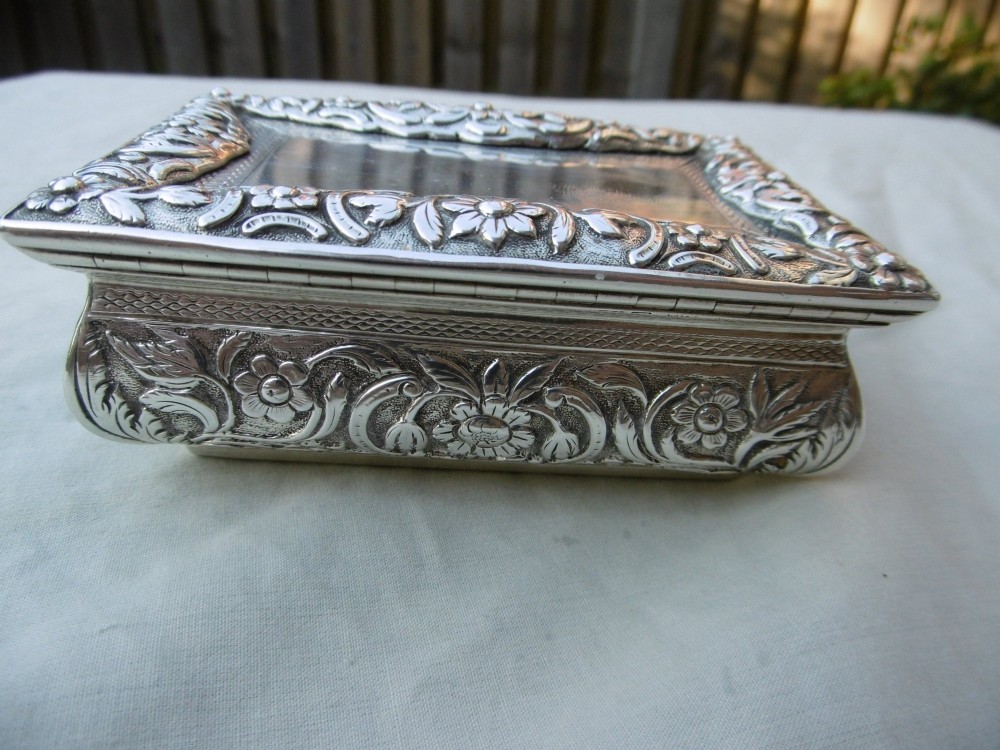 A rectangular William IV sterling silver table snuff box featuring heavily chased floral borders and an engine-turned lid with a plain central cartouche. View IV
