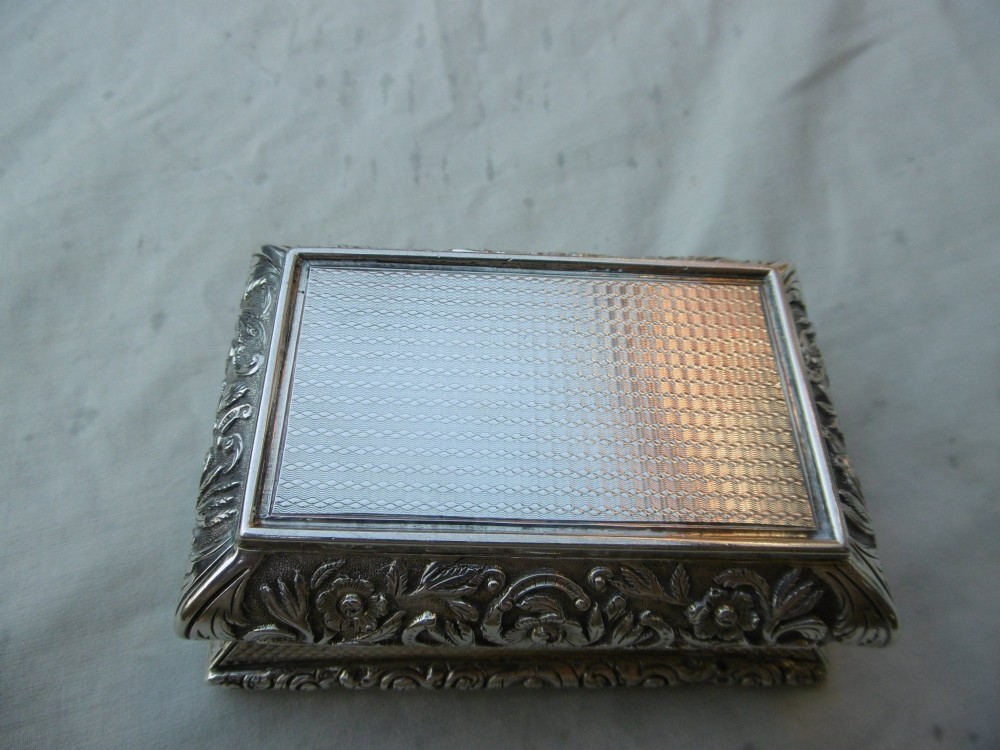 A rectangular William IV sterling silver table snuff box featuring heavily chased floral borders and an engine-turned lid with a plain central cartouche. View V