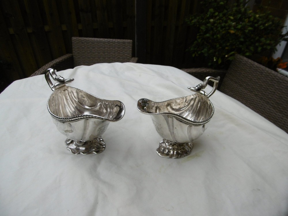 A pair of 18th-century Georgian sterling silver sauce boats featuring fluted shell bodies, serpent handles, and pedestal bases.