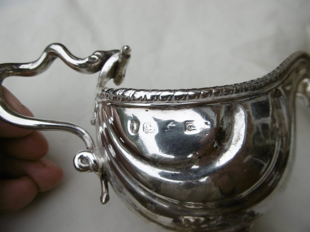 A pair of 18th-century Georgian sterling silver sauce boats featuring fluted shell bodies, serpent handles, and pedestal bases. View V
