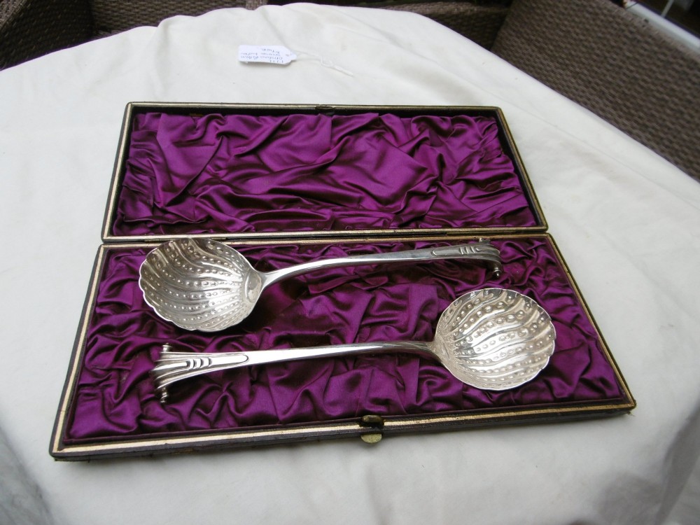A pair of Georgian sterling silver ladles with Onslow pattern scroll handles and shell-shaped bowls resting inside a velvet-lined presentation box.