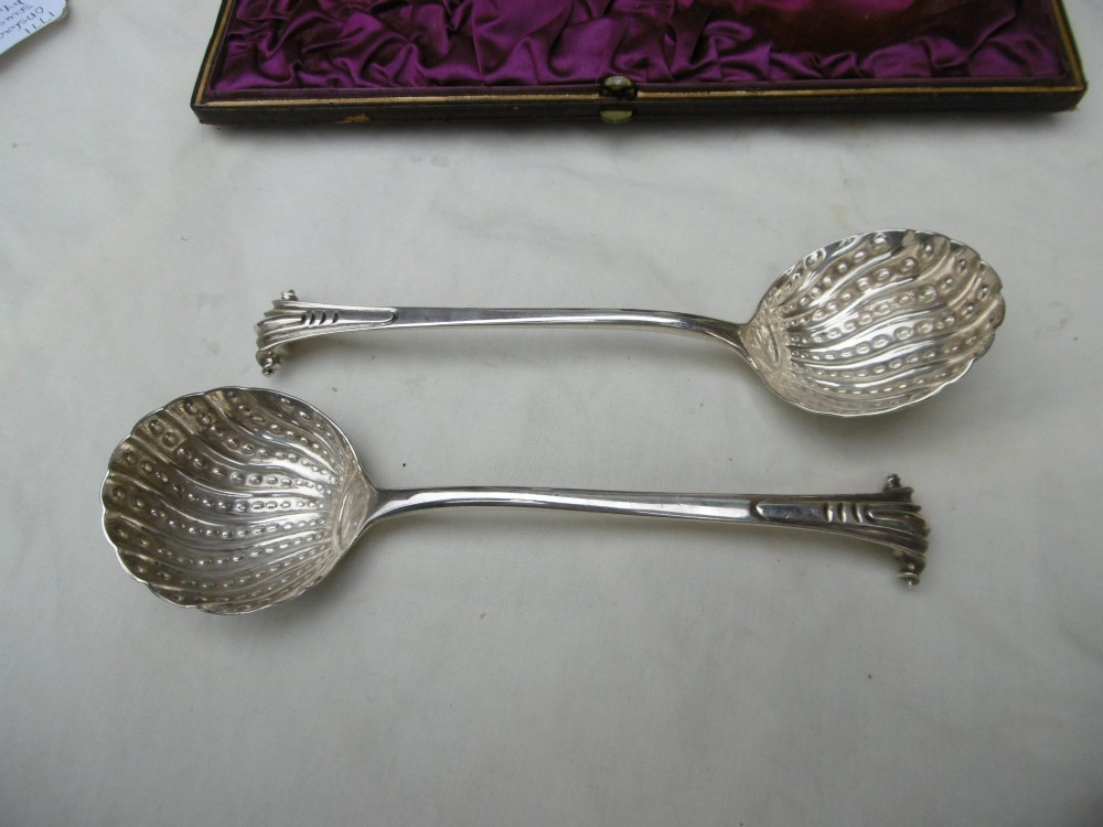 A pair of Georgian sterling silver ladles with Onslow pattern scroll handles and shell-shaped bowls resting inside a velvet-lined presentation box. View II