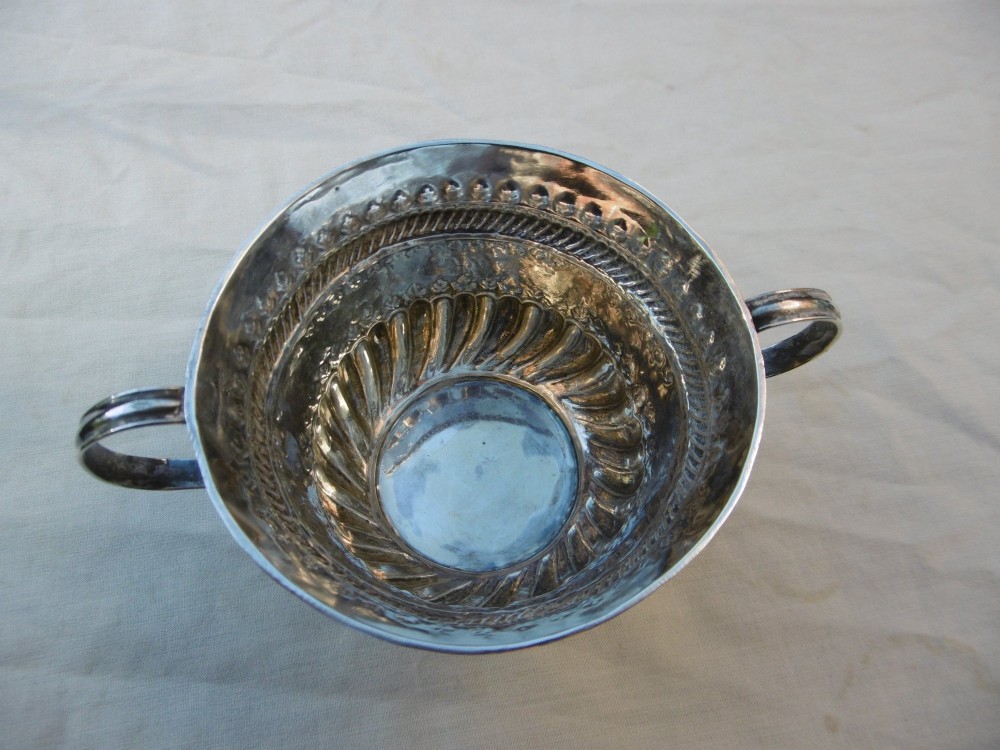 A George I Britannia standard silver porringer with twin scroll handles, fluted lower body decoration, and gadrooned banding. View V