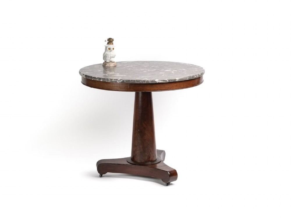 A circular 19th-century French gueridon table featuring a grey veined marble top resting on a tapered mahogany pedestal with a tri-form base.