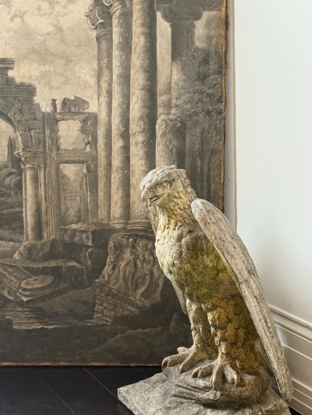 A weathered composite stone eagle sculpture with spread wings mounted on a square plinth base. View II