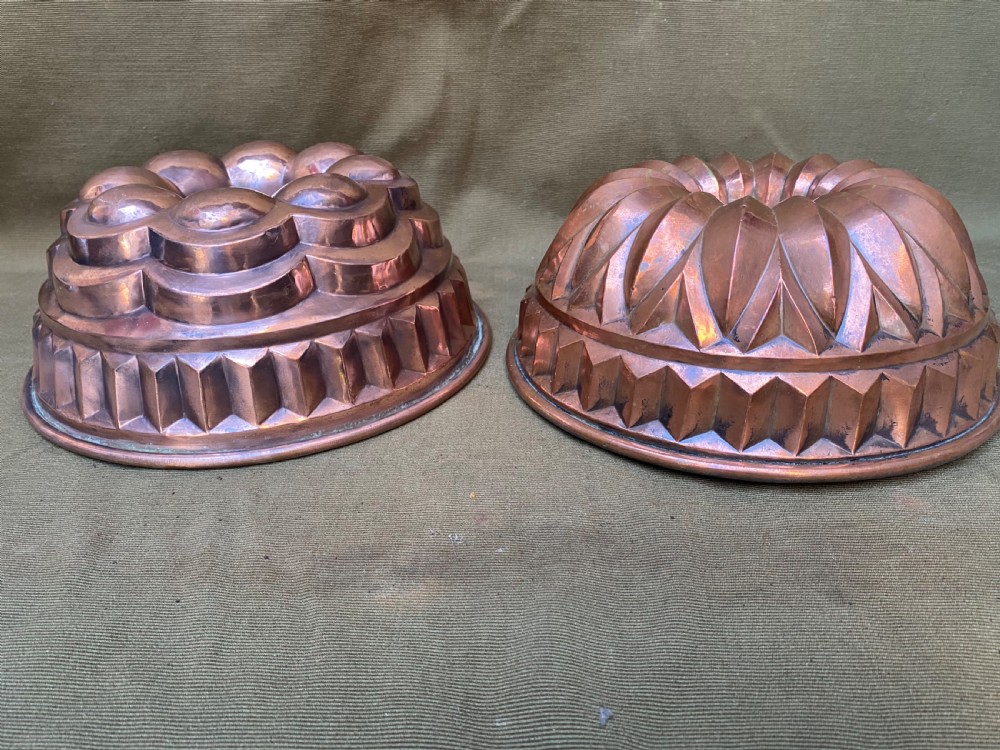 A pair of circular antique copper cake moulds featuring fluted and lobed geometric relief patterns.