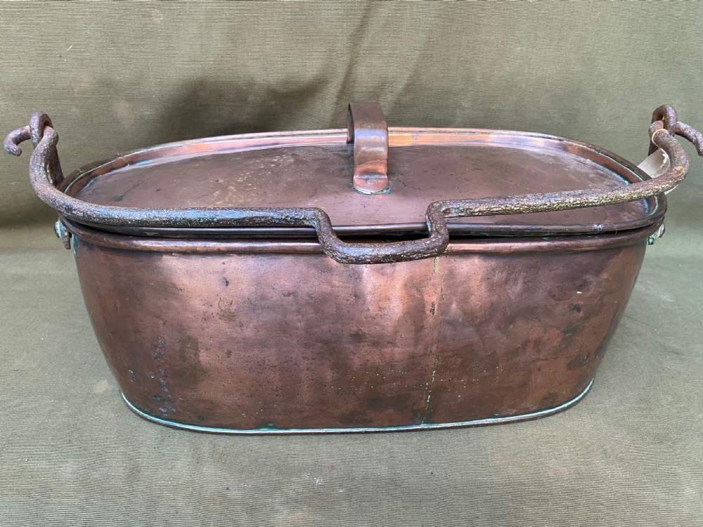 An oval antique copper fish kettle with a fitted copper lid and heavy wrought iron handles on either side.