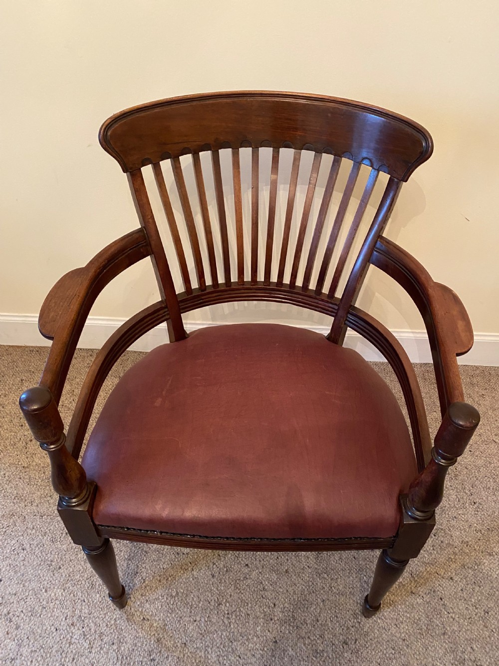 A pair of mahogany club armchairs featuring vertical slat backrests, curved arms with turned supports, and reddish-brown leather upholstered seats with stud detailing. View X