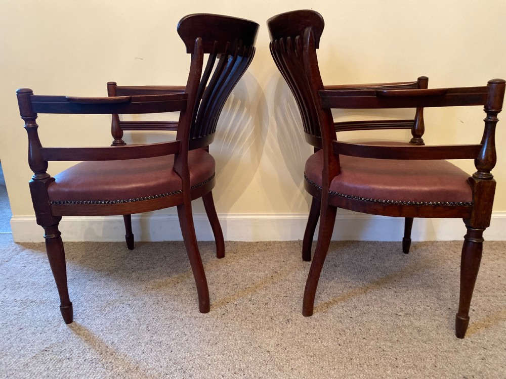 A pair of mahogany club armchairs featuring vertical slat backrests, curved arms with turned supports, and reddish-brown leather upholstered seats with stud detailing. View XII