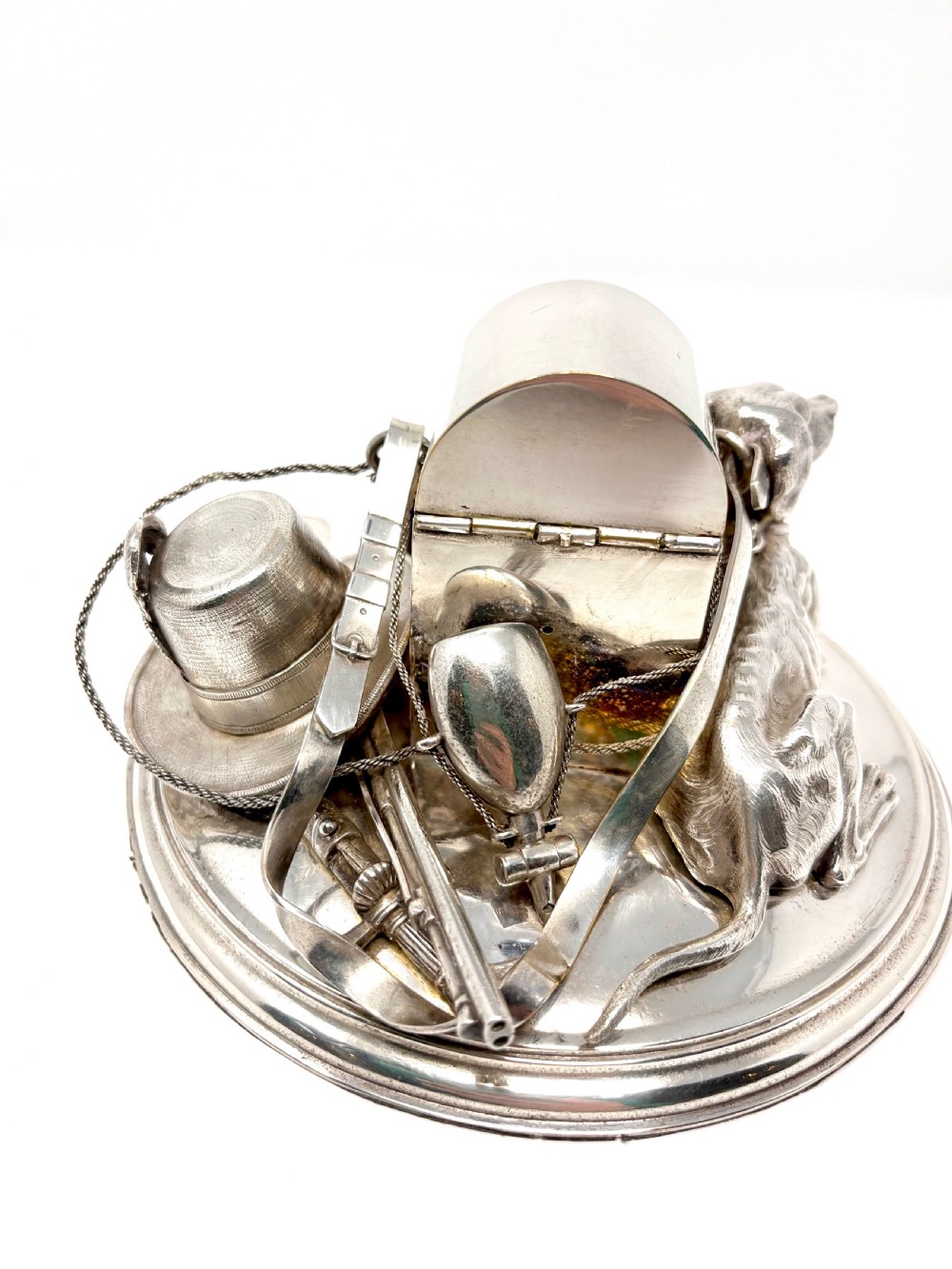 A Victorian silver-plated desk inkstand featuring a sculpted reclining hunting hound next to a game bag and domed ink container on a circular stepped base. View IV