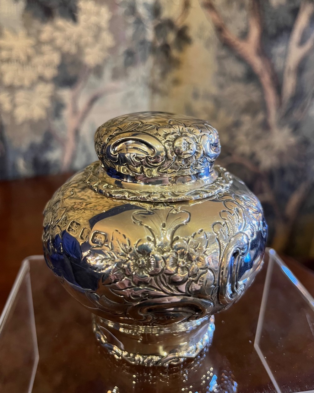 A bulbous antique silver tea caddy featuring hand-chased floral repousse decoration, visible hallmarks, and a fitted domed cap. View III