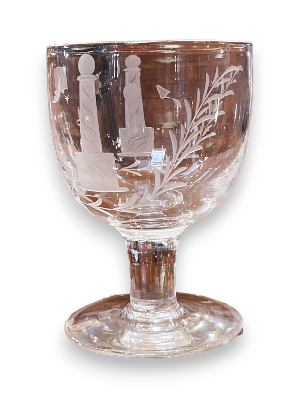 A clear Georgian glass goblet featuring detailed wheel-engraved Masonic iconography, supported by a short stem and wide circular foot.