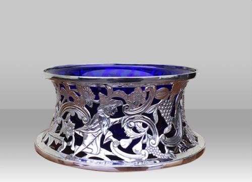 fig 1. A pierced sterling silver spool-shaped dish ring decorated with carved figures and scrollwork, fitted with a cobalt blue glass liner.