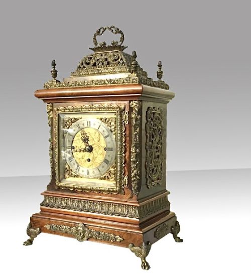 fig 1. An ornate wooden triple fusee bracket clock featuring decorative gilt-brass mounts, a silvered chapter ring, and a pierced basket top with a brass carrying handle.