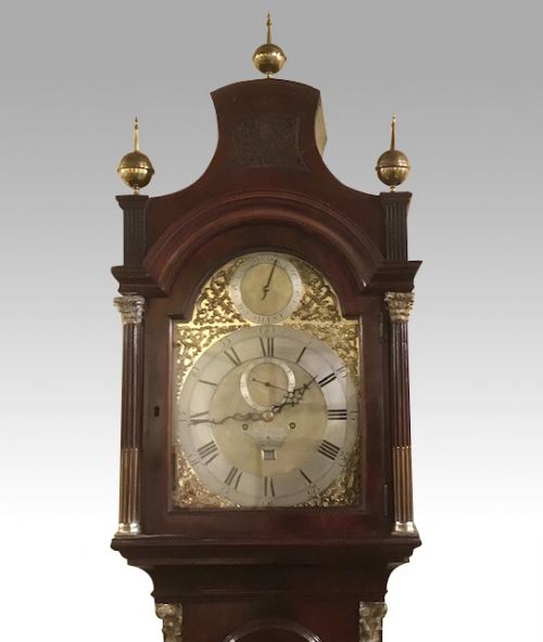 fig 1. A George III mahogany longcase clock featuring an arched brass dial with spandrels, fluted Corinthian columns, and a pagoda hood topped with brass finials.