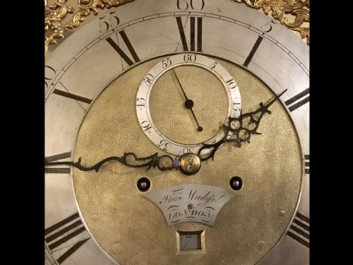 fig 3. A George III mahogany longcase clock featuring an arched brass dial with spandrels, fluted Corinthian columns, and a pagoda hood topped with brass finials.