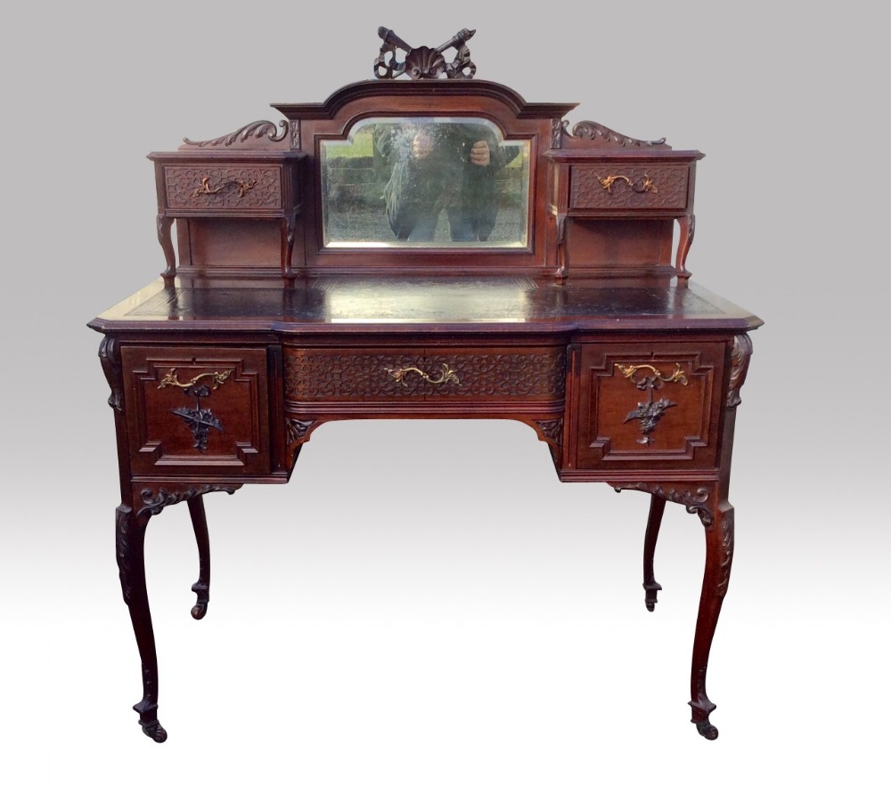 An antique dark mahogany bonheur du jour writing desk featuring a mirrored superstructure with small side drawers, cabriole legs, brass handles, and carved decorative panels.