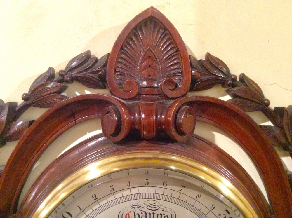 A carved mahogany Victorian aneroid wall barometer featuring a circular dial with weather markings framed by carved leaf motifs and scrollwork. View II