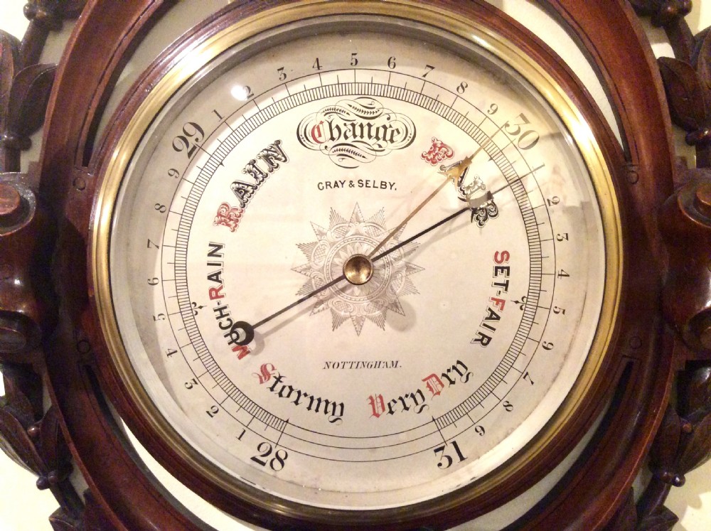 A carved mahogany Victorian aneroid wall barometer featuring a circular dial with weather markings framed by carved leaf motifs and scrollwork. View III