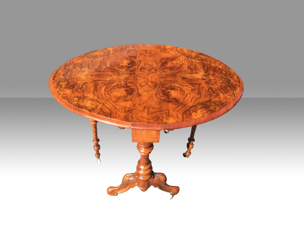 A Victorian burr walnut baby Sutherland table with folded leaves, barley-twist supports, carved feet, and ceramic castors. View V