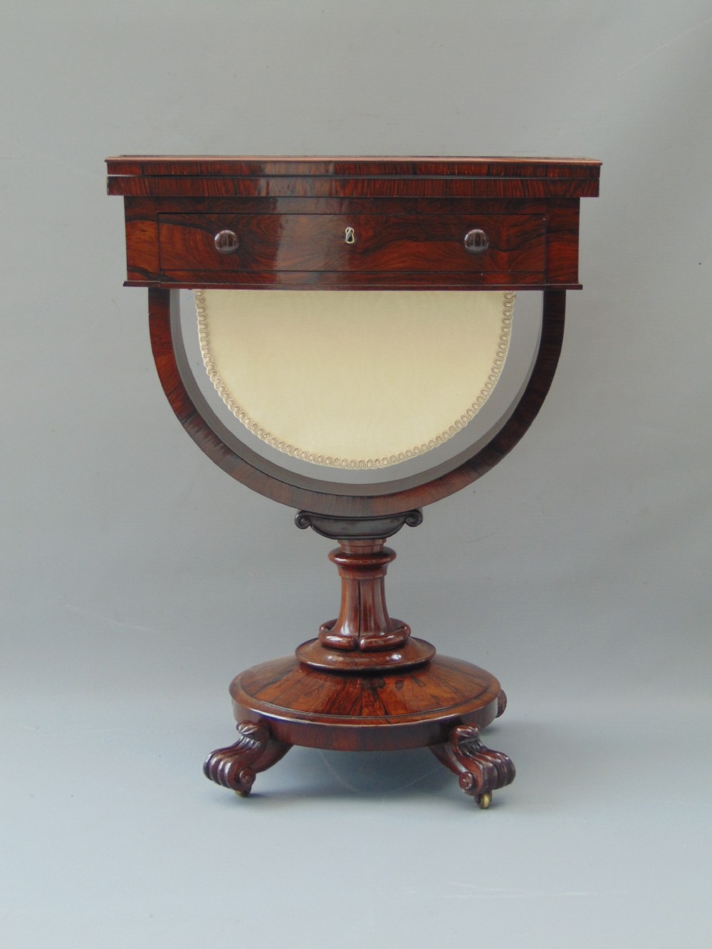 A William IV rosewood sewing and games table with a fold-over top, single drawer, suspended cream fabric work basket, and turned pedestal base with scroll feet. View VII