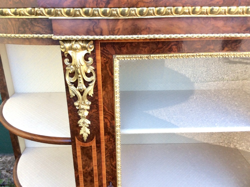An antique burr walnut credenza featuring a central glazed door flanked by open curved display shelves and ornate gilt metal mounts. View VIII