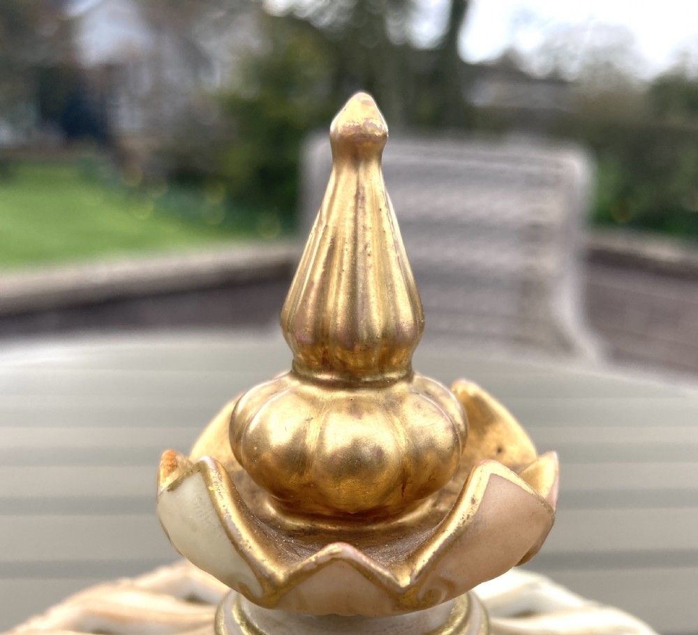 A bulbous Royal Worcester blush ivory porcelain pot pourri vase featuring hand-painted floral blooms, basketweave moulded relief details, and a decorative finial cover. View VI