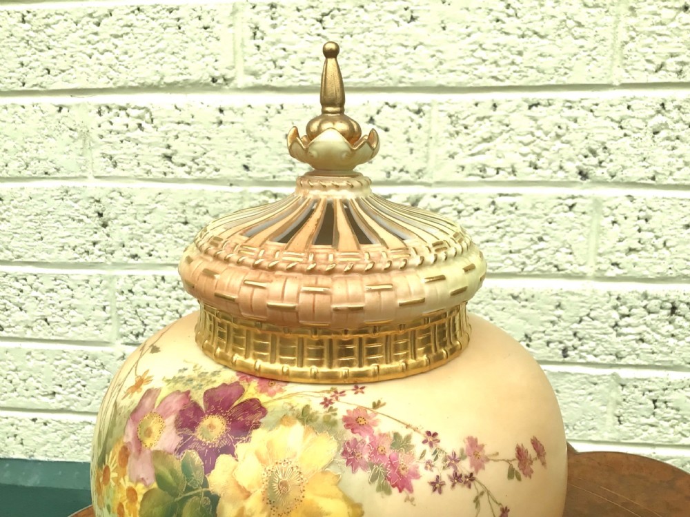 A globular Royal Worcester blush ivory pot pourri vase featuring hand-painted floral motifs, basketweave relief detail, and a pierced gilded lid. View X