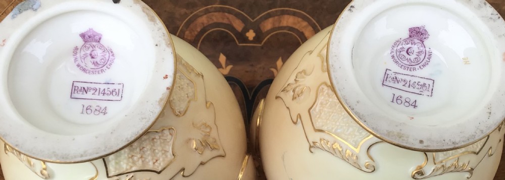 A pair of Victorian Royal Worcester blush ivory porcelain vases decorated with hand-painted floral motifs, twin gilt handles, and matching pointed finial lids. View VI