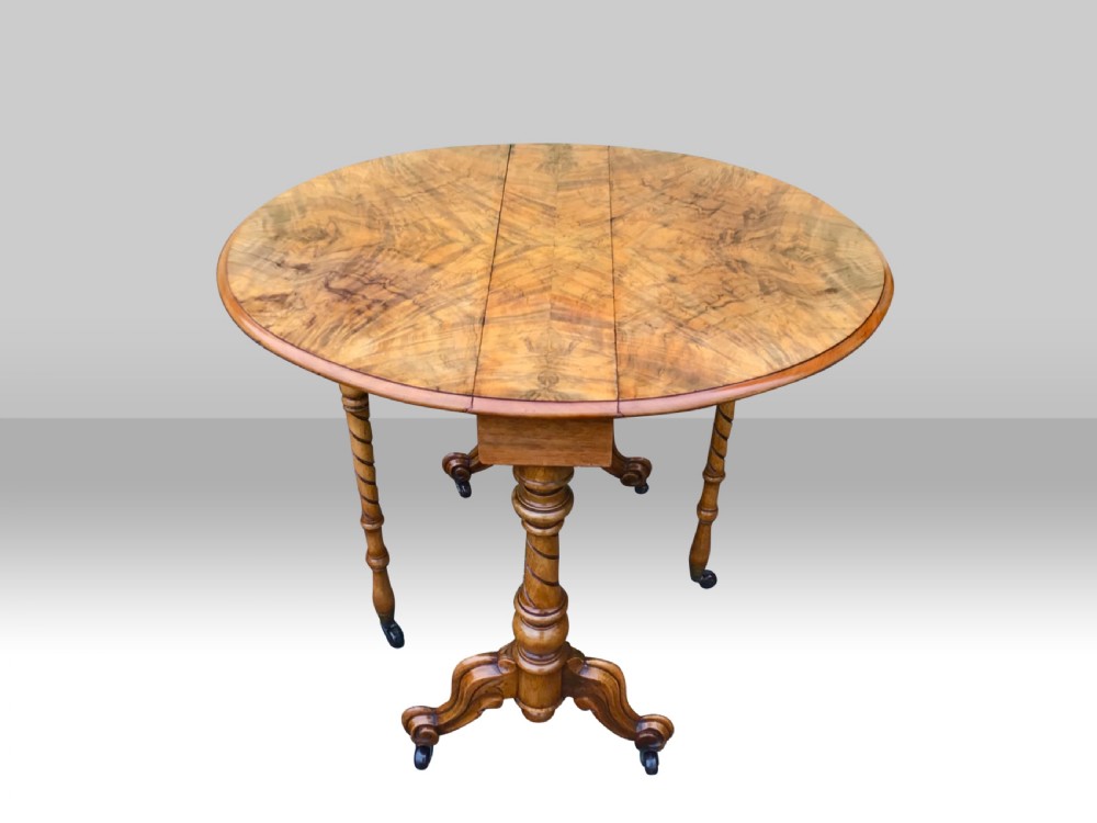 An antique figured walnut Sutherland drop-leaf table featuring spiral turned supports and carved legs on castors. View IV