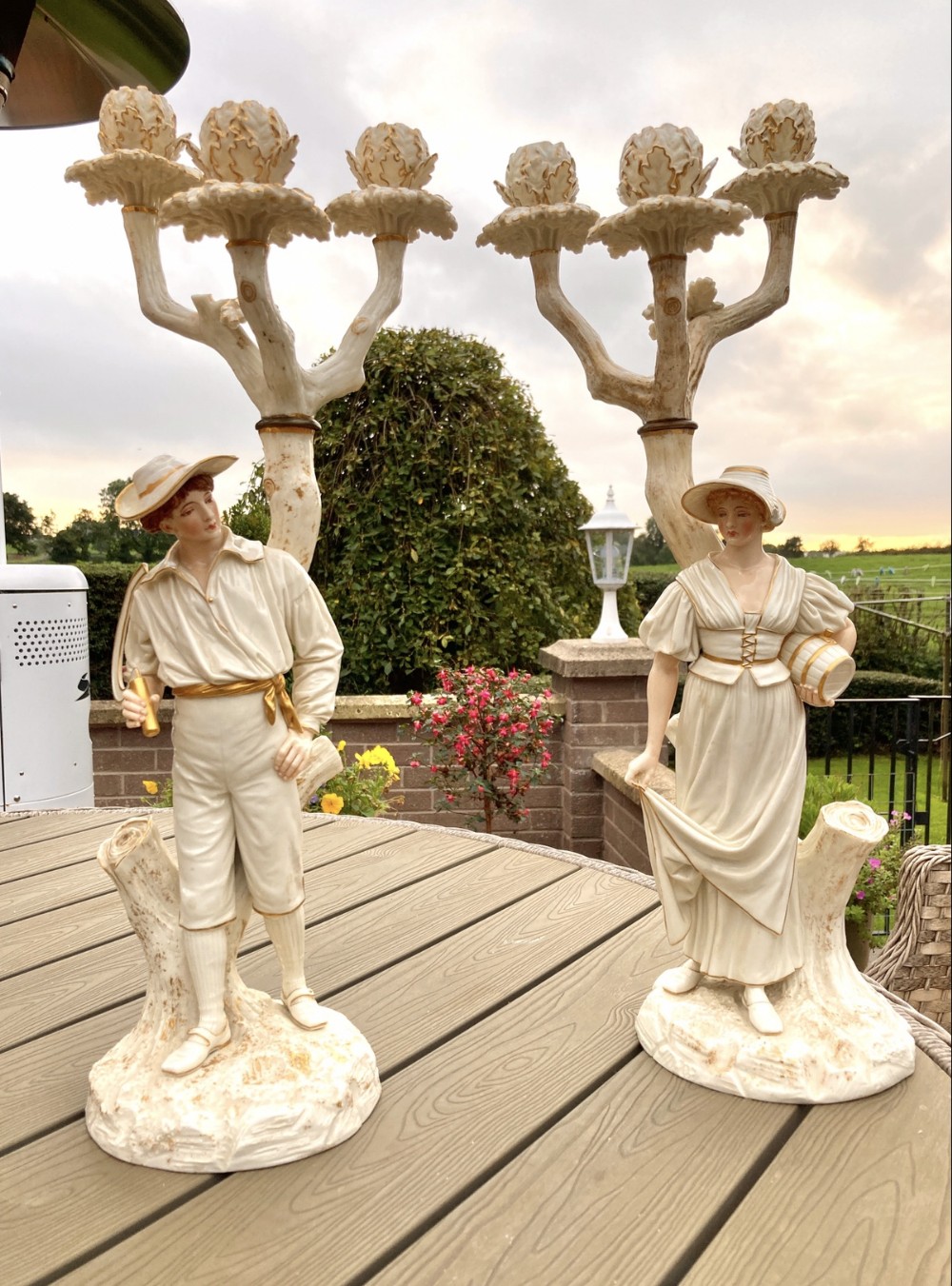 A pair of Victorian Royal Worcester porcelain candelabra shaped as rustic male and female figures beside tree trunks supporting candle sconces.