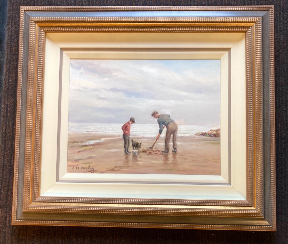 An oil painting on canvas depicting figures and a dog on a sandy shoreline, presented in a stepped gilded and textured wooden frame.