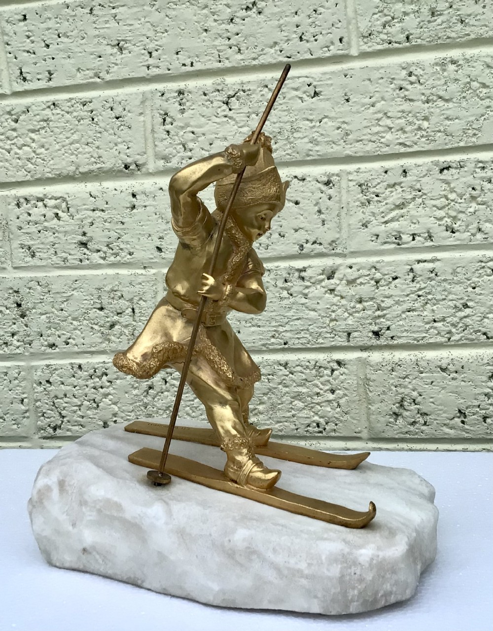 A gilded bronze figure of a skier holding a pole, mounted on a carved white marble base simulating snow.